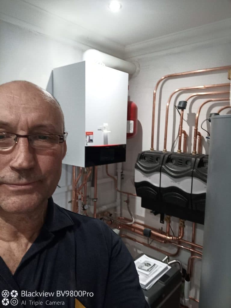 Home Comfort Assured Renewables engineer in a plant room checking manifolds, cylinder and pipework while fault finding